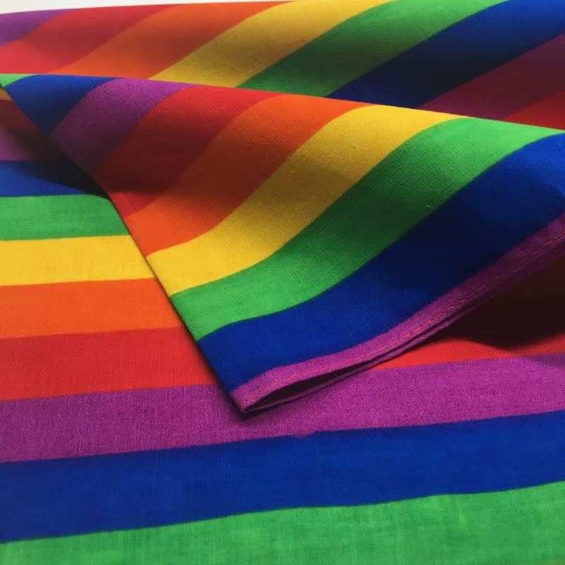 Detailansicht des gefalteten Regenbogen-Bandanas. Durch die lockere Faltung des Stoffes verlaufen die farbintensiven Pride-Streifen hier diagonal, während die sauber vernähte Saumkante des Tuches im Vordergrund deutlich sichtbar ist.