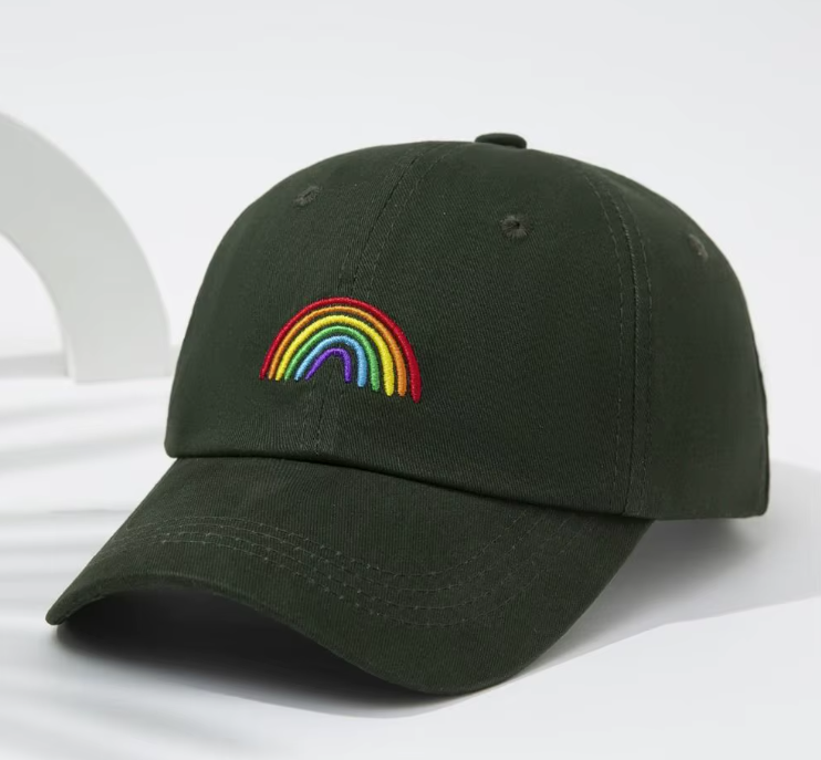 Eine dunkelgrüne Baseballkappe mit einem kleinen, farbintensiven Regenbogen auf der Stirnseite. Eine praktische und unaufgeregte Kopfbedeckung für queere Sichtbarkeit im Alltag.