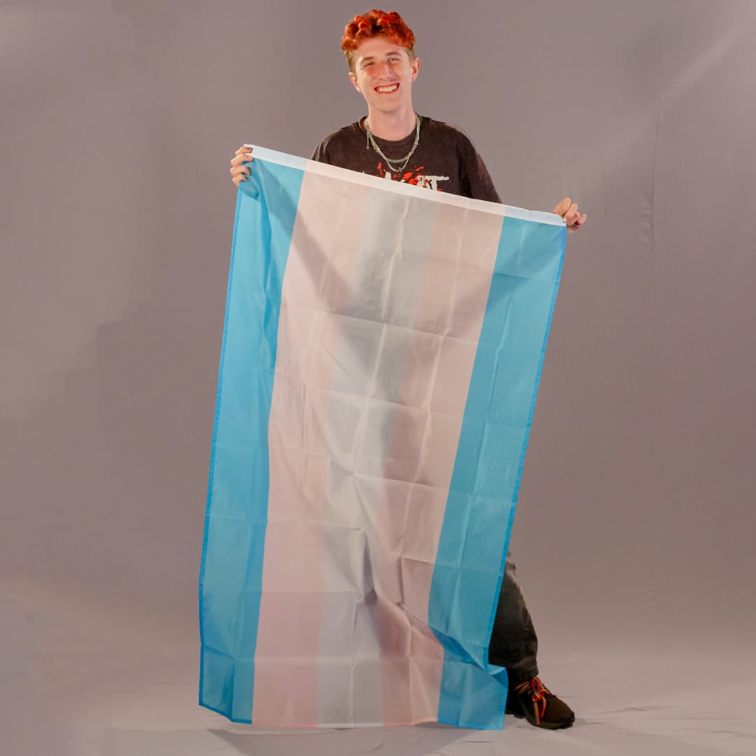 Justus Kornmesser, einer der Initiatoren von PrideLAB, hält die große Trans-Pride-Flagge in 150x90 cm senkrecht vor sich.