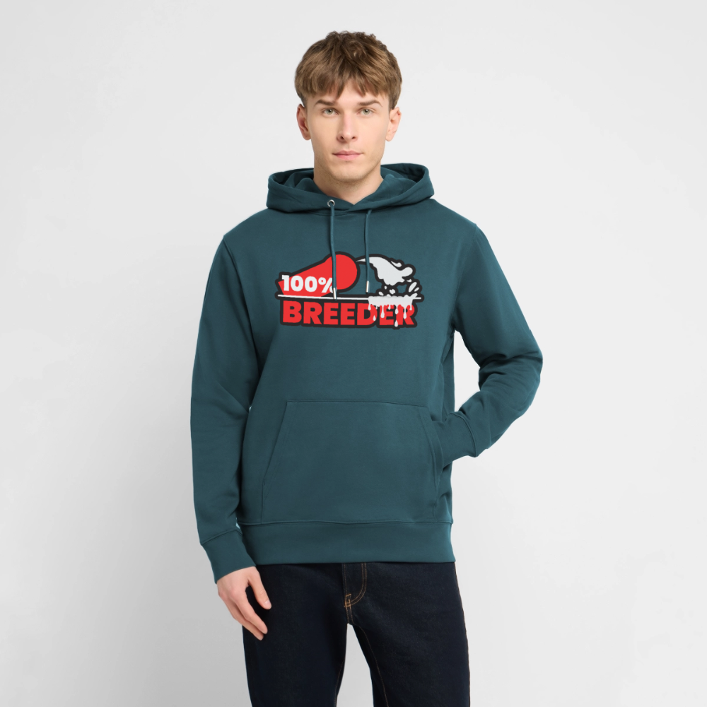 Attraktiver Mann in dunklem Petrol Bio-Hoodie mit dominantem 100% Breeder Motiv – klares Statement für aktive und dominante Player