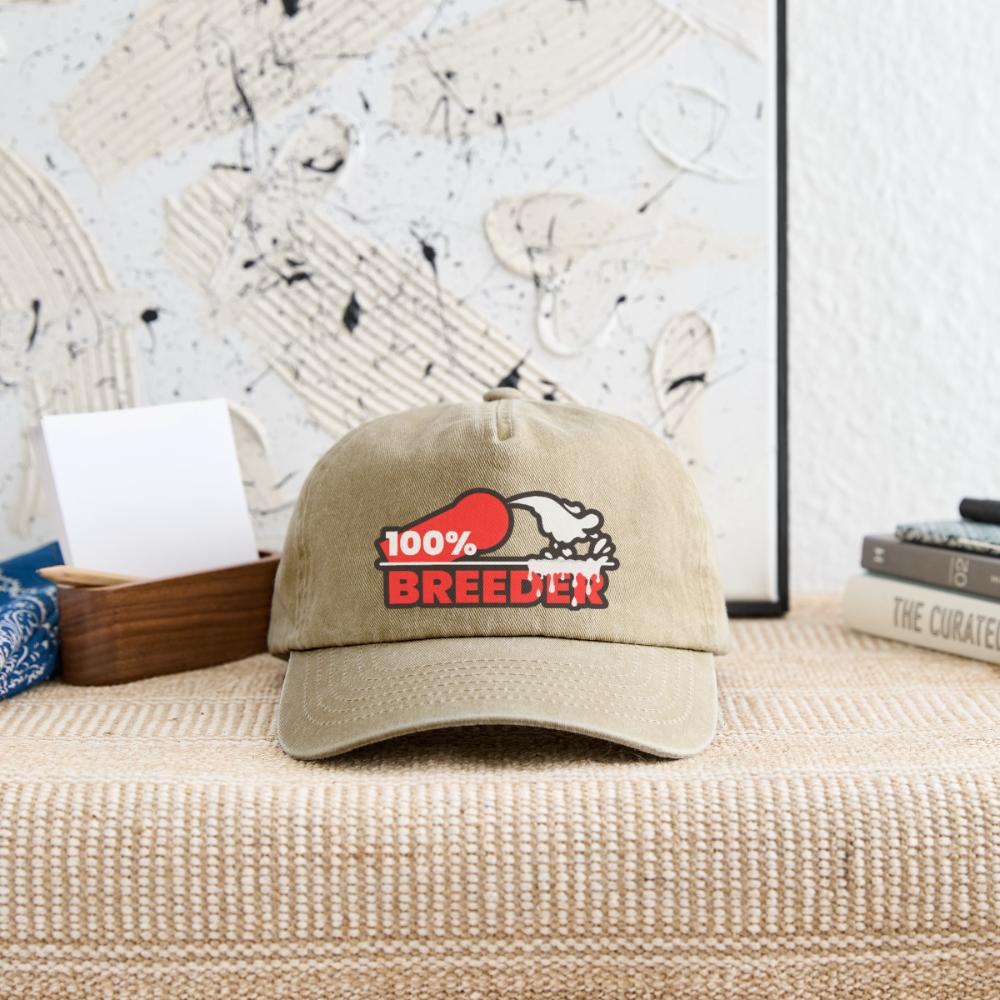 Vintage beige Cap mit "100% Breeder" Kink Fetish Design hängt an der Wand – für aktive und dominante Männer