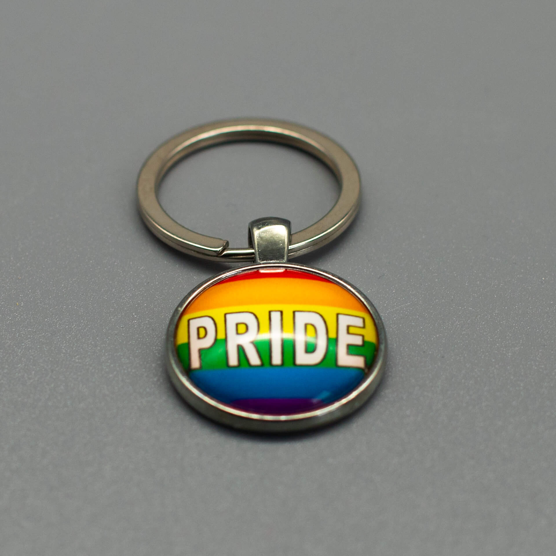 Nahaufnahme eines silbernen LGBTQ Accessoire Schlüsselanhängers mit Glasdom und dem weißen Schriftzug PRIDE auf Regenbogenhintergrund.